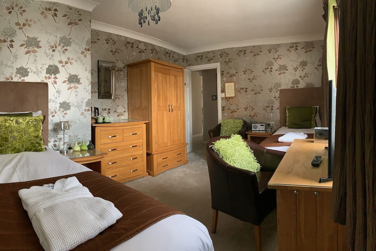 Een slaapkamer met een bed, een houten garderobe, een bureau met stoel en een spiegel.