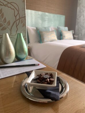 A hotel room with a neatly made bed, a bedside table with a tray of chocolate coins, and two vases on the wall. - Ramsey House (Haverfordwest)