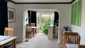 A dining area with wooden chairs and a table, a kitchen area with a sink and cabinets, and a view of a garden through a glass door. - Ramsey House (Haverfordwest)