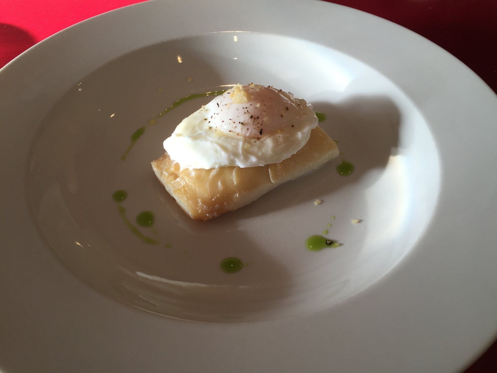 A white plate with a piece of food topped with a poached egg and a garnish of green sauce.