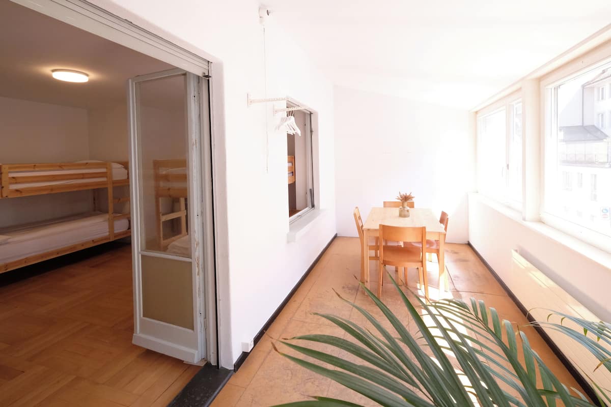A room with a wooden bunk bed, a dining area with a table and chairs, and a potted plant.