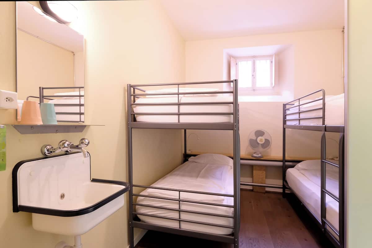 A dormitory room with bunk beds, a sink, and a window.