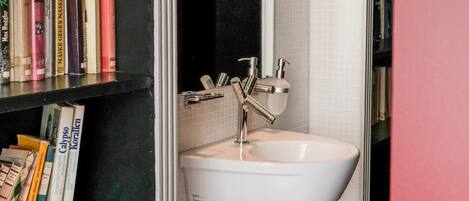 Un baño con un lavabo blanco, un espejo y una estantería con libros.