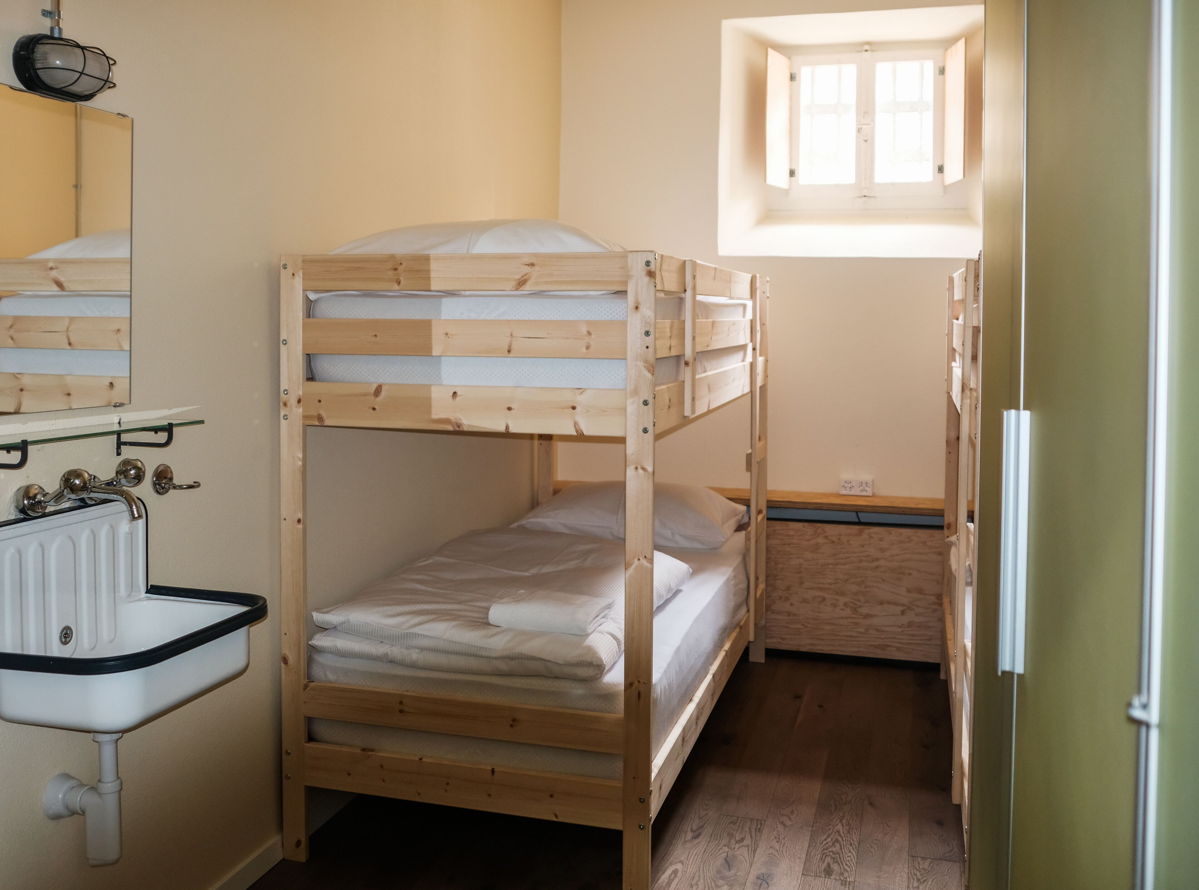 A small, compact room with two bunk beds, a wooden sink, and a window providing natural light.