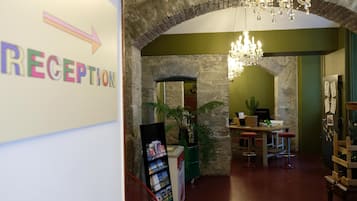 Ett entréområde med en skylt som visar vägen till receptionen, en kristallkrona, en valvformad öppning i sten, en växt och en bardisk med barstolar.