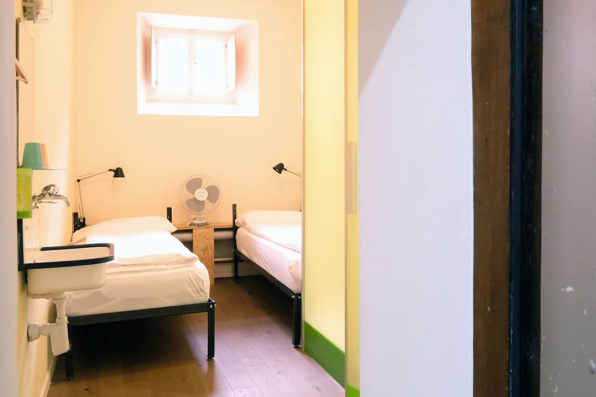 A narrow hallway with two beds, a fan, and a window.