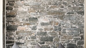 A room with a stone wall, a grey sofa with cushions, and wooden flooring. - Barabas - Hostel (Lucerne)