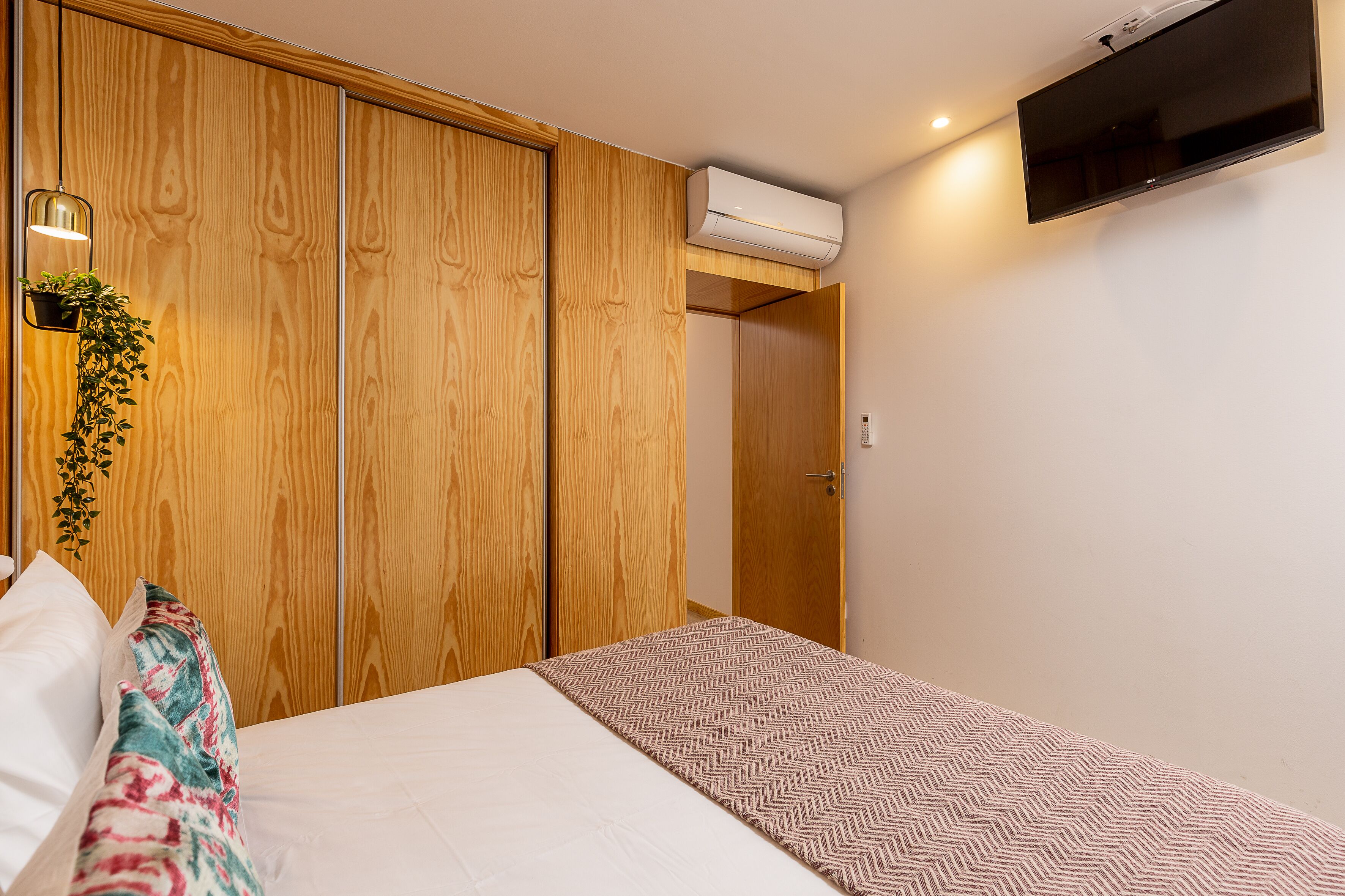 Une chambre à coucher comprenant un lit, une armoire en bois, un téléviseur fixé au mur et un appareil de climatisation.