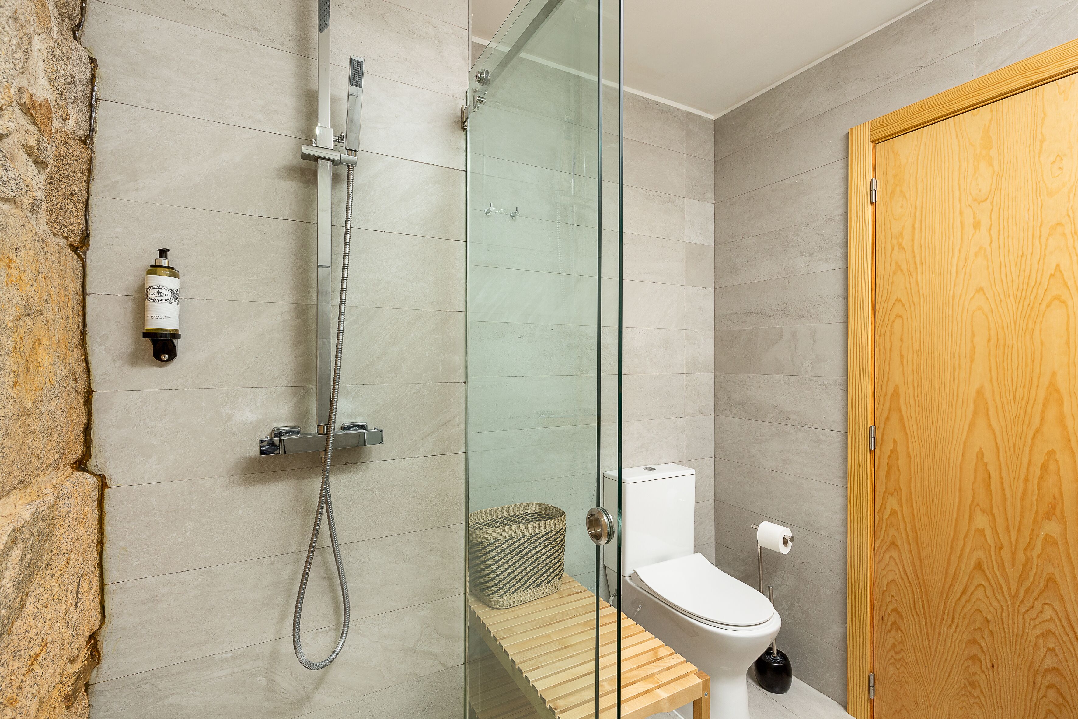 Une salle de bain moderne avec une douche à parois de verre, un banc en bois, des toilettes et une porte en bois.