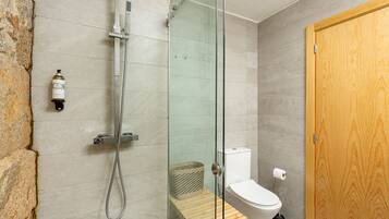 Un baño moderno con ducha acristalada, un banco de madera, inodoro y puerta de madera.