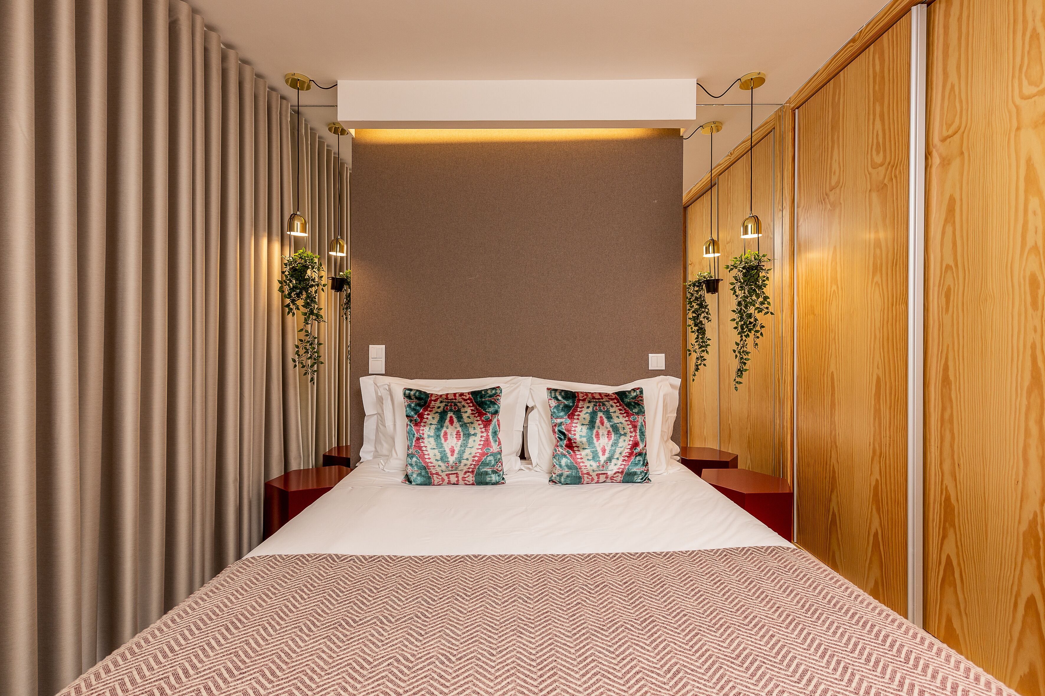 A hotel room with a large bed, two nightstands, a wooden wardrobe, and hanging plants.