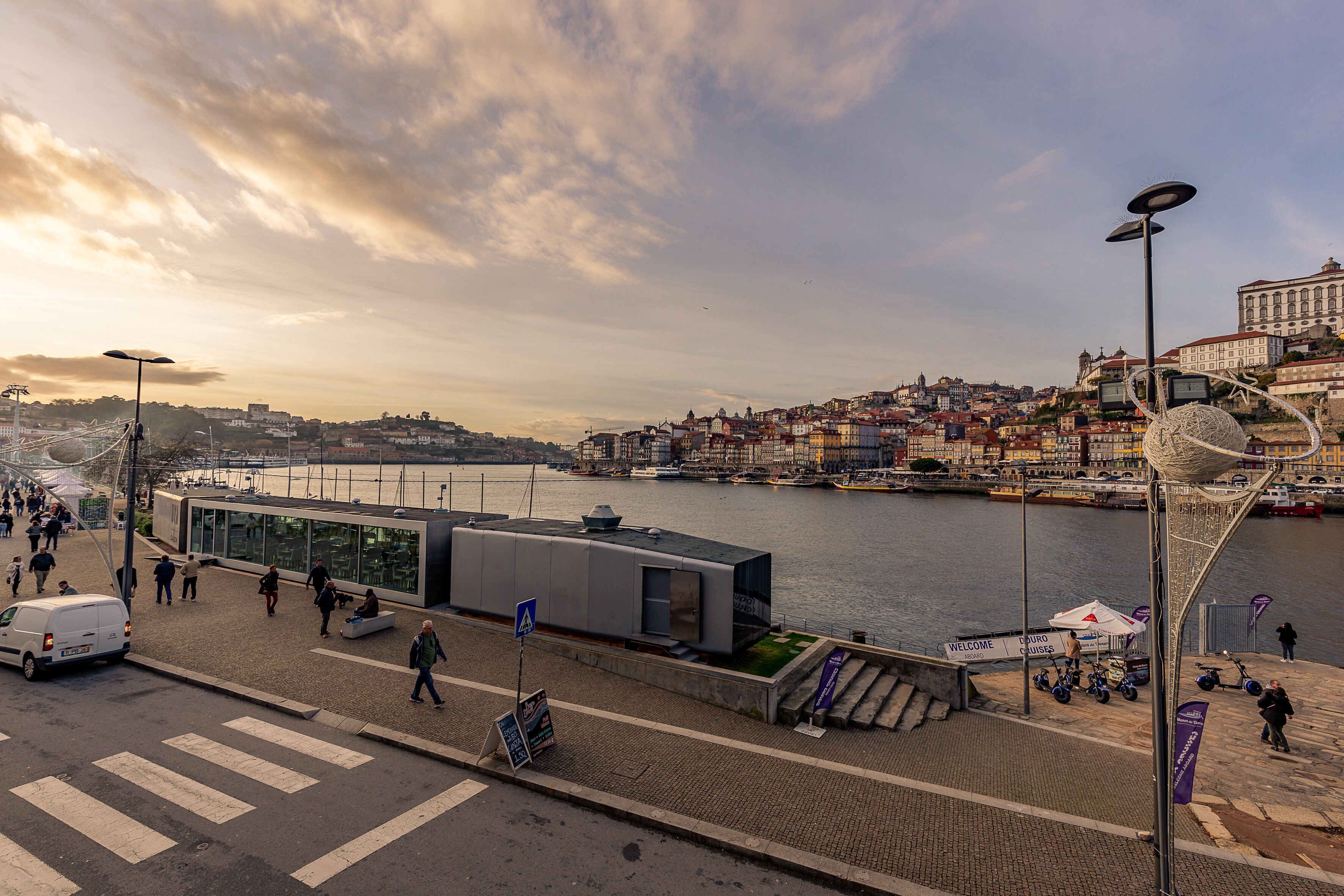 A waterfront promenade with a modern building, a river, and boats.