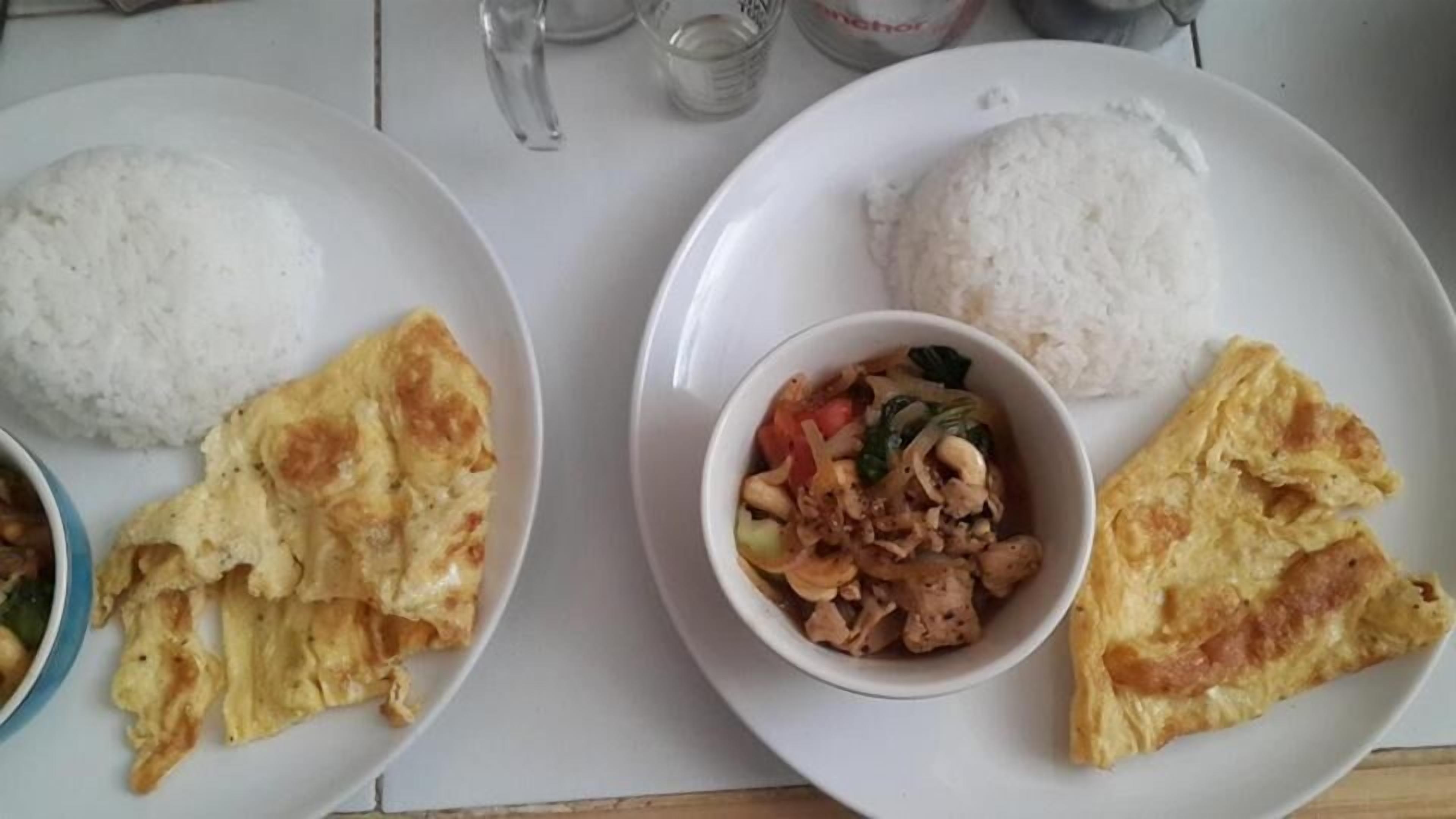 Deux assiettes de nourriture : l’une contient du riz et un bol de légumes sautés, et l’autre, du riz et des tranches d’omelette.
