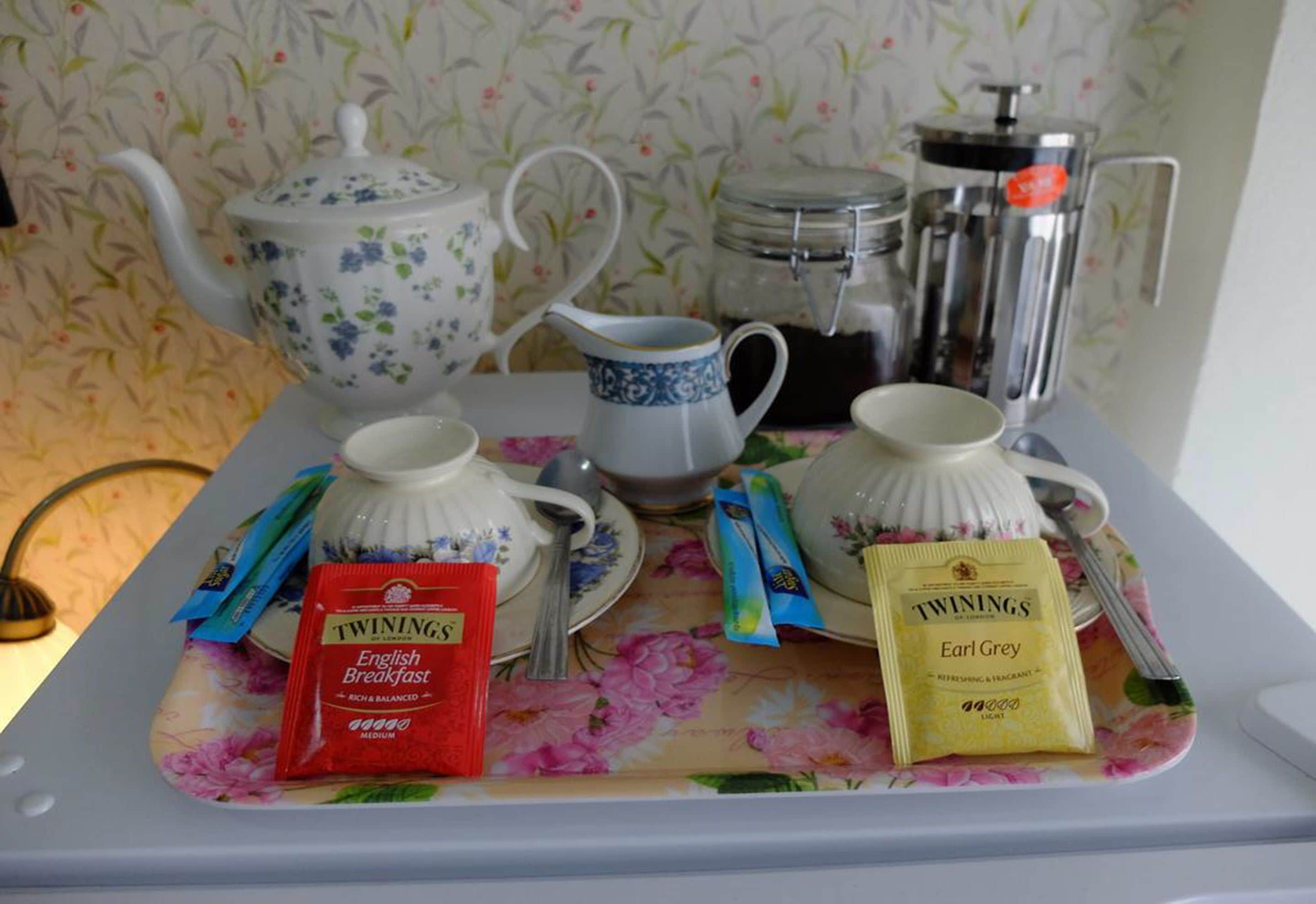 En frukostuppsättning med ett blommigt bordsduksöverdrag, en tekanna, en kaffekanna och teportioner av Twinings Earl Grey.