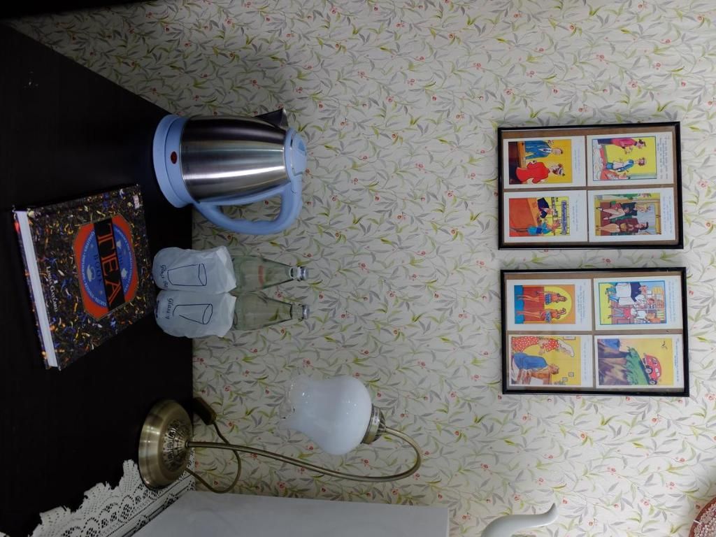 Une pièce avec un papier peint à motifs, une bande dessinée encadrée accrochée au mur, une bouilloire, une lampe et un livre posé sur une table.