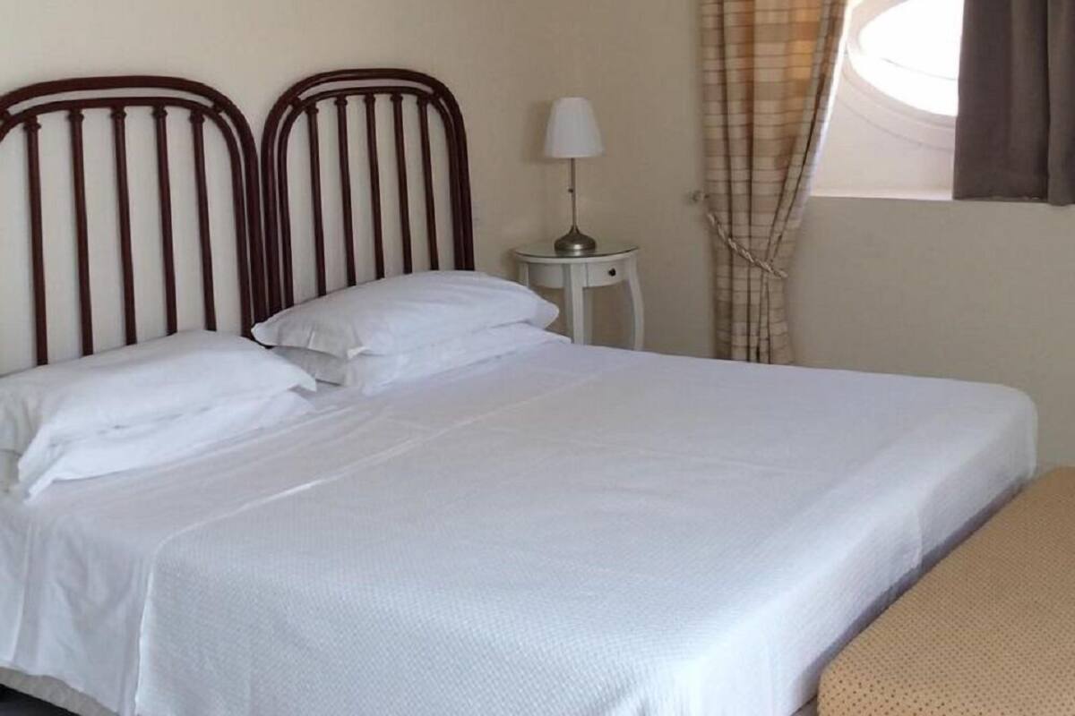 Un lit simple avec une tête de lit en bois, une table de chevet avec une lampe et une fenêtre avec des rideaux.