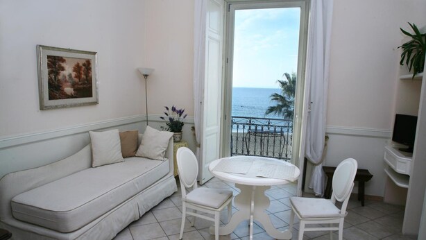 A balcony with a white sofa, two white chairs, a small round table, and a view of the sea. - Palazzetto Florio (Castellabate)