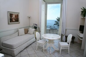 Un balcón con un sofá blanco, dos sillas blancas, una mesita redonda y vista al mar.