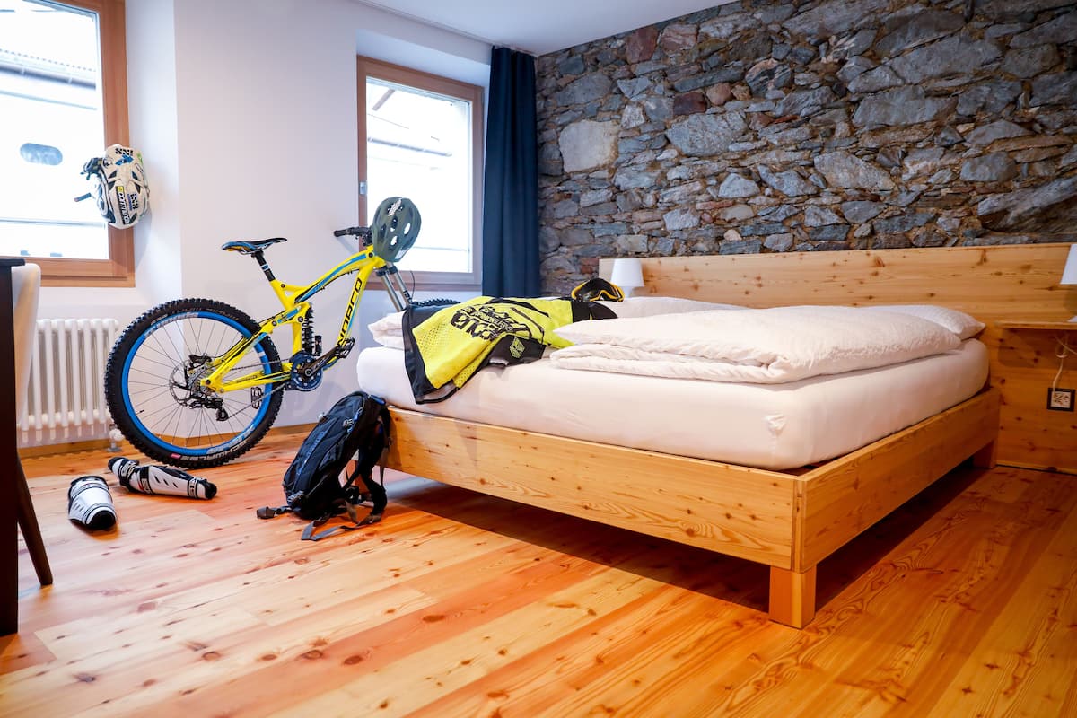 Un lit en bois, un mur en pierre, un vélo et un casque posés sur le sol.