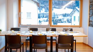 Un comedor con una mesa dispuesta para cuatro, grandes ventanales con vistas a una montaña nevada y una pared de piedra en un lateral.