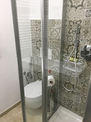A bathroom with a glass shower enclosure, a toilet, and a showerhead. - Il Peccato Originale (Matera)