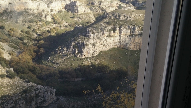 Vista a través de una ventana que muestra un paisaje montañoso con acantilados rocosos y vegetación escasa.