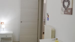 Una habitación pequeña y limpia, con un aparador blanco, una mesita de noche y un radiador.