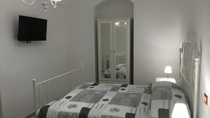 Un dormitorio con cama, televisión montada en la pared, lámpara de noche y espejo.