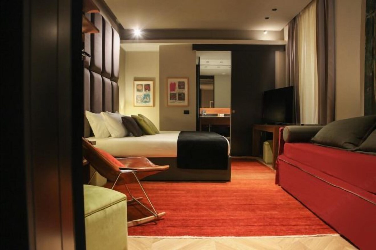 A hotel room with a bed, a red sofa, a television, and a small table.