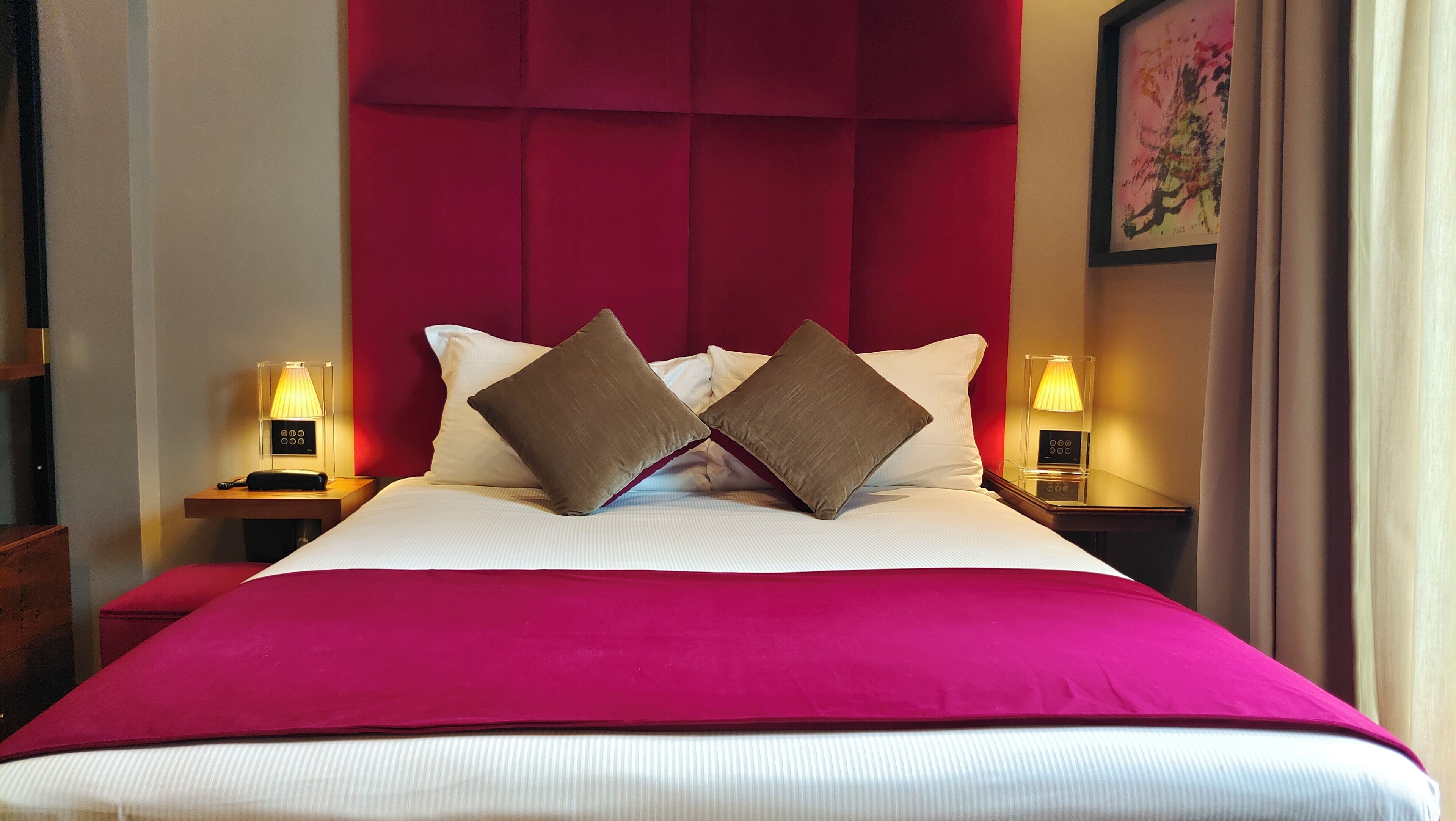 Une chambre d’hôtel avec un grand lit, une tête de lit rouge, deux lampes de chevet et un plaid rouge.