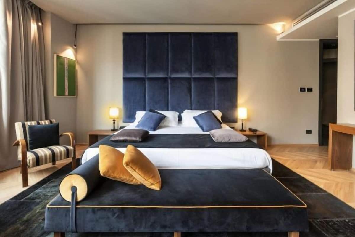Una moderna camera d'albergo con un letto grande, due comodini, una sedia e un'ampia finestra.