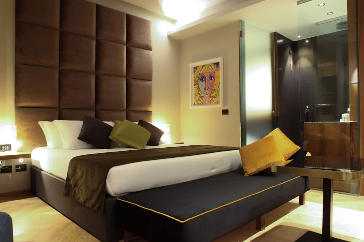 Una camera d'albergo moderna con un letto grande, un comodino e un box doccia in vetro.