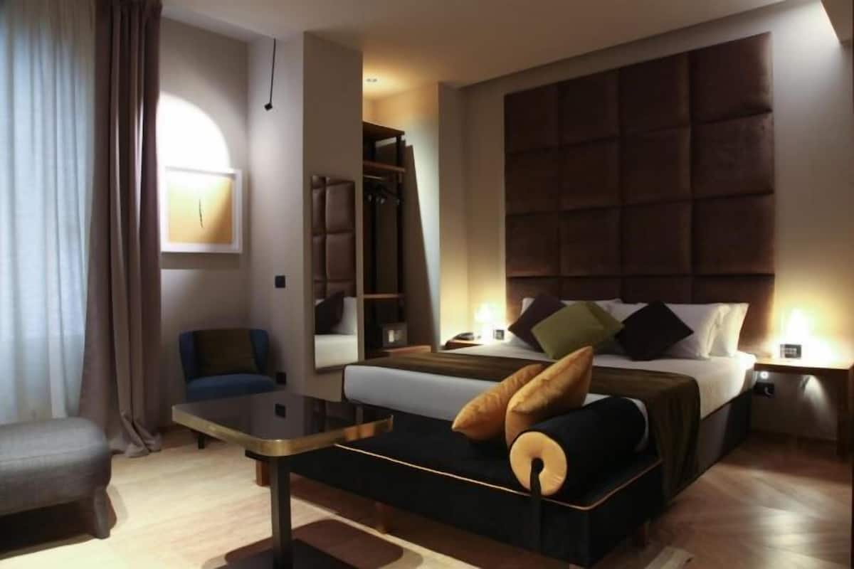 Una camera d'hotel moderna con un letto grande, una zona salotto con un tavolo e vista sulla città.