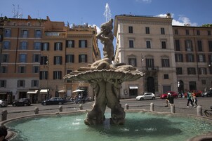Una fontana con una statua al centro, circondata da un'area pavimentata e con edifici sullo sfondo.