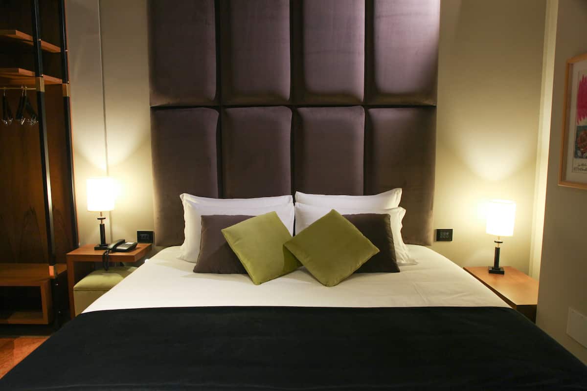 Una camera d'albergo con un letto grande, due comodini con lampade e un armadio.