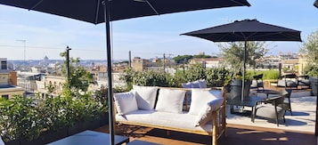 Una terrazza sul tetto con divano, sedie e ombrelloni, con vista sulla città.