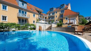 A swimming pool surrounded by multi-story buildings with balconies, a clear blue sky, and a wooden deck with a chair. - Apparthotel Steiger Bad Schandau (Bad Schandau)