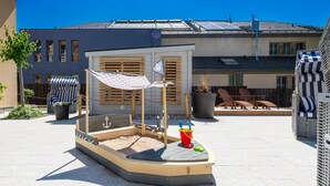 A children's play area with a sandbox, a small boat, and a shaded seating area. - Apparthotel Steiger Bad Schandau (Bad Schandau)