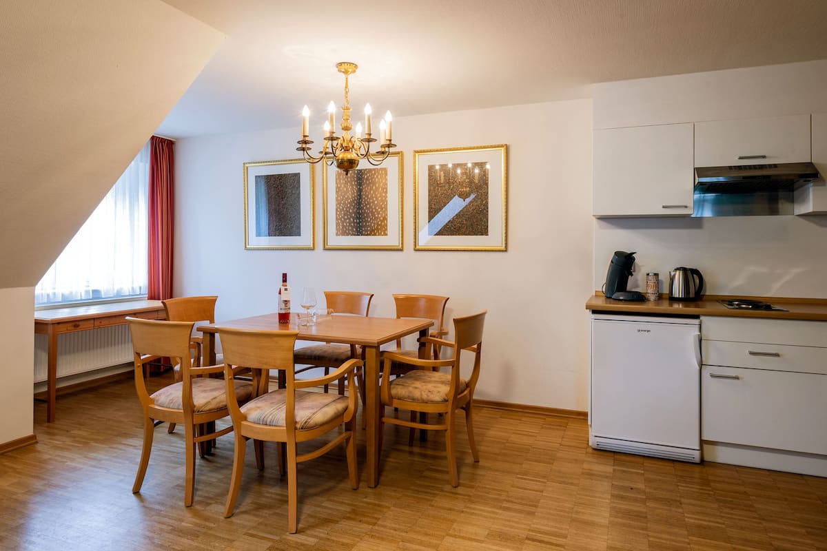 A dining area with a wooden table and chairs, a chandelier, and framed artwork on the wall.
