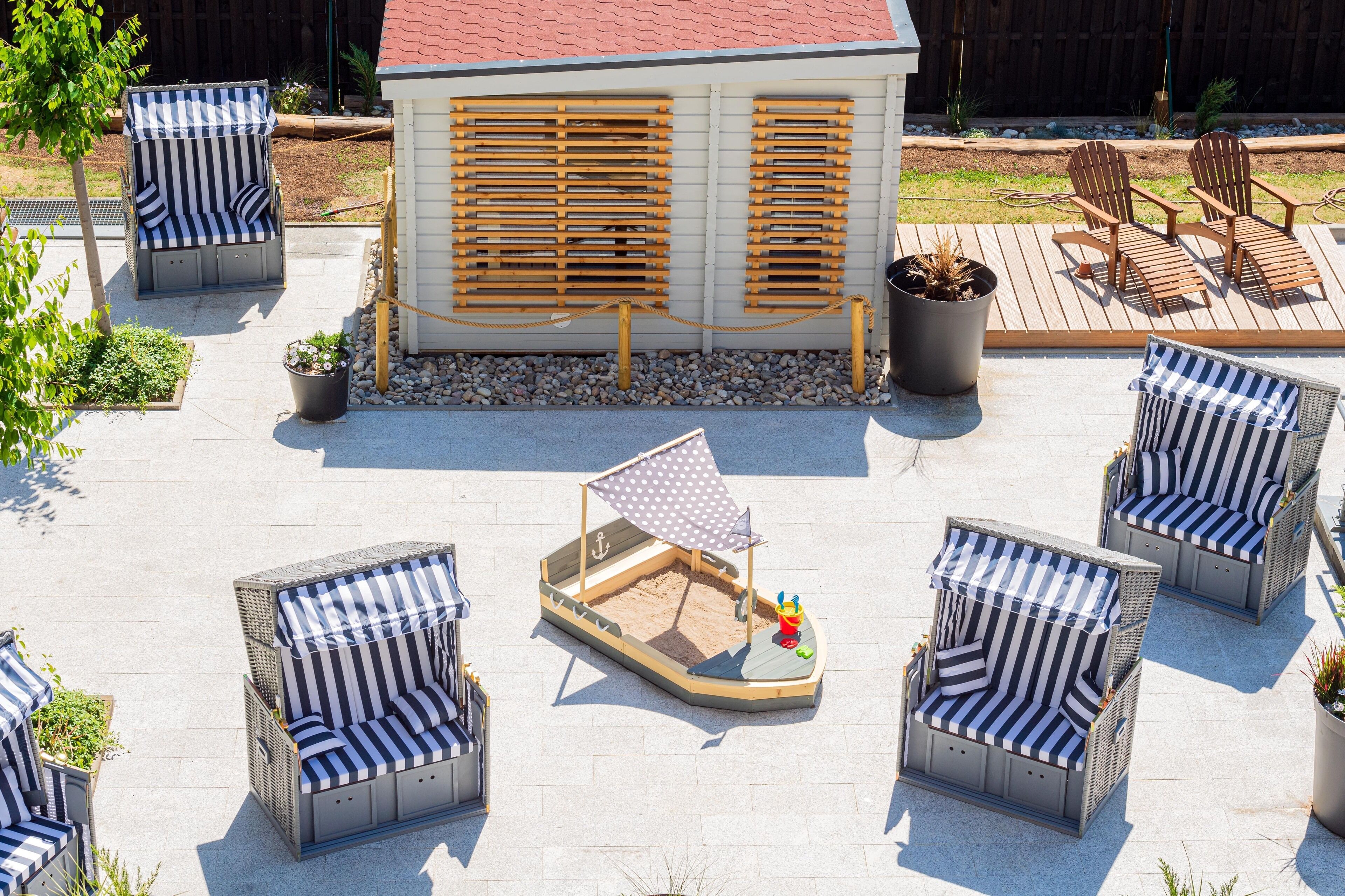 Eine Terrasse mit Sitzgelegenheiten im Freien, darunter gestreifte Stühle und ein kleiner, bootförmiger Tisch mit Segel.
