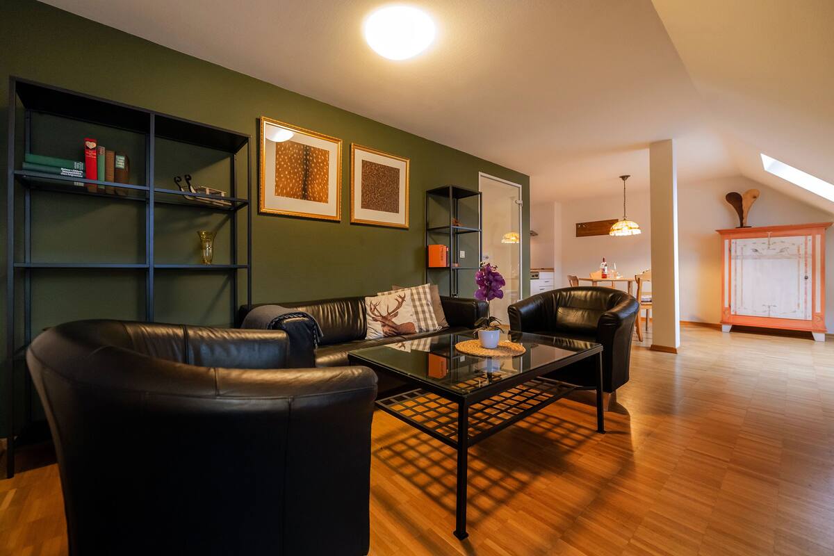 A modern living room with a leather sofa, a glass coffee table, and a bookshelf against a green wall.