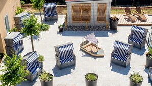 An outdoor seating area with wicker chairs and tables, surrounded by potted plants and a small wooden structure. - Apparthotel Steiger Bad Schandau (Bad Schandau)
