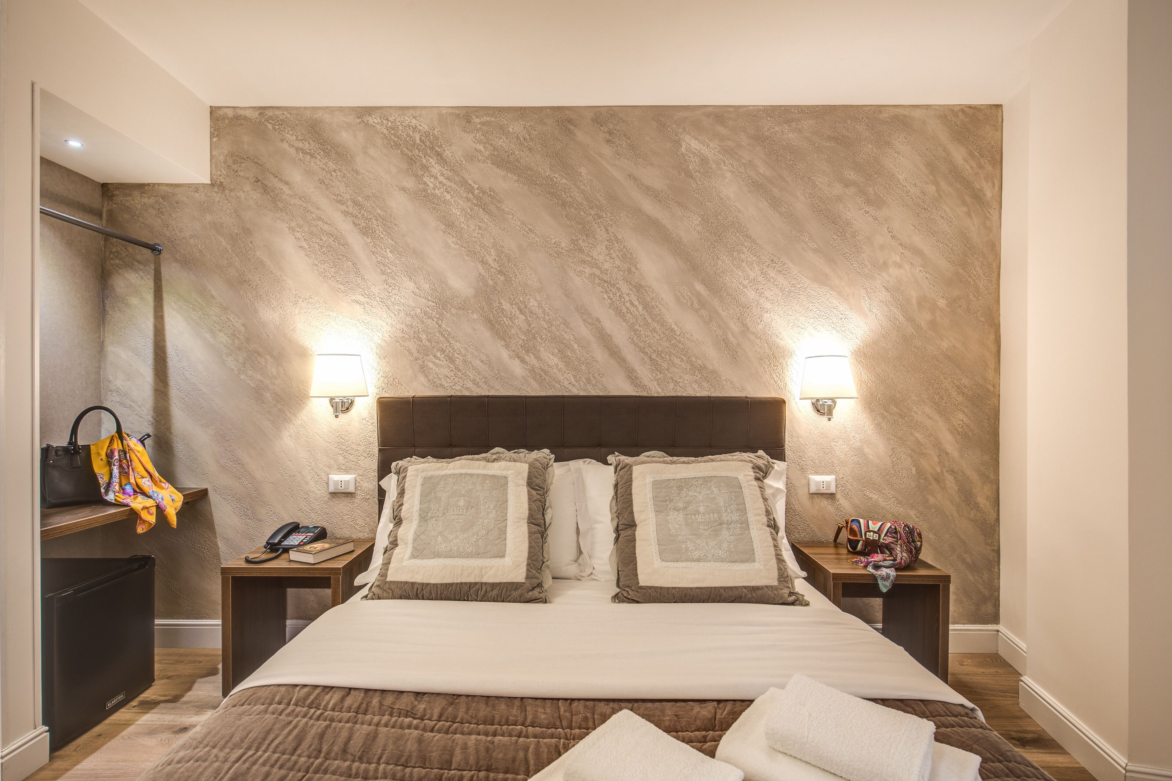 A hotel room with a large bed, two bedside tables, a nightstand, a wardrobe, and a mirror.
