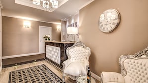 A luxurious lobby with a grand chandelier, a clock, and two ornate chairs. - River Luxury Suites (Rome)