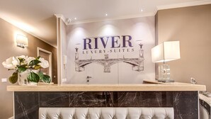 A reception area with a marble counter, a white tufted chair, and a wall with the text "RIVER LUXURY SUITES". - River Luxury Suites (Rome)