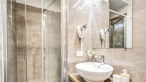 A modern bathroom with a glass-enclosed shower, a white sink with a wooden countertop, and a mirror above the sink. - River Luxury Suites (Rome)