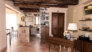 Una cocina rústica con vigas a la vista, un comedor con mesa de madera y un televisor montado en la pared.