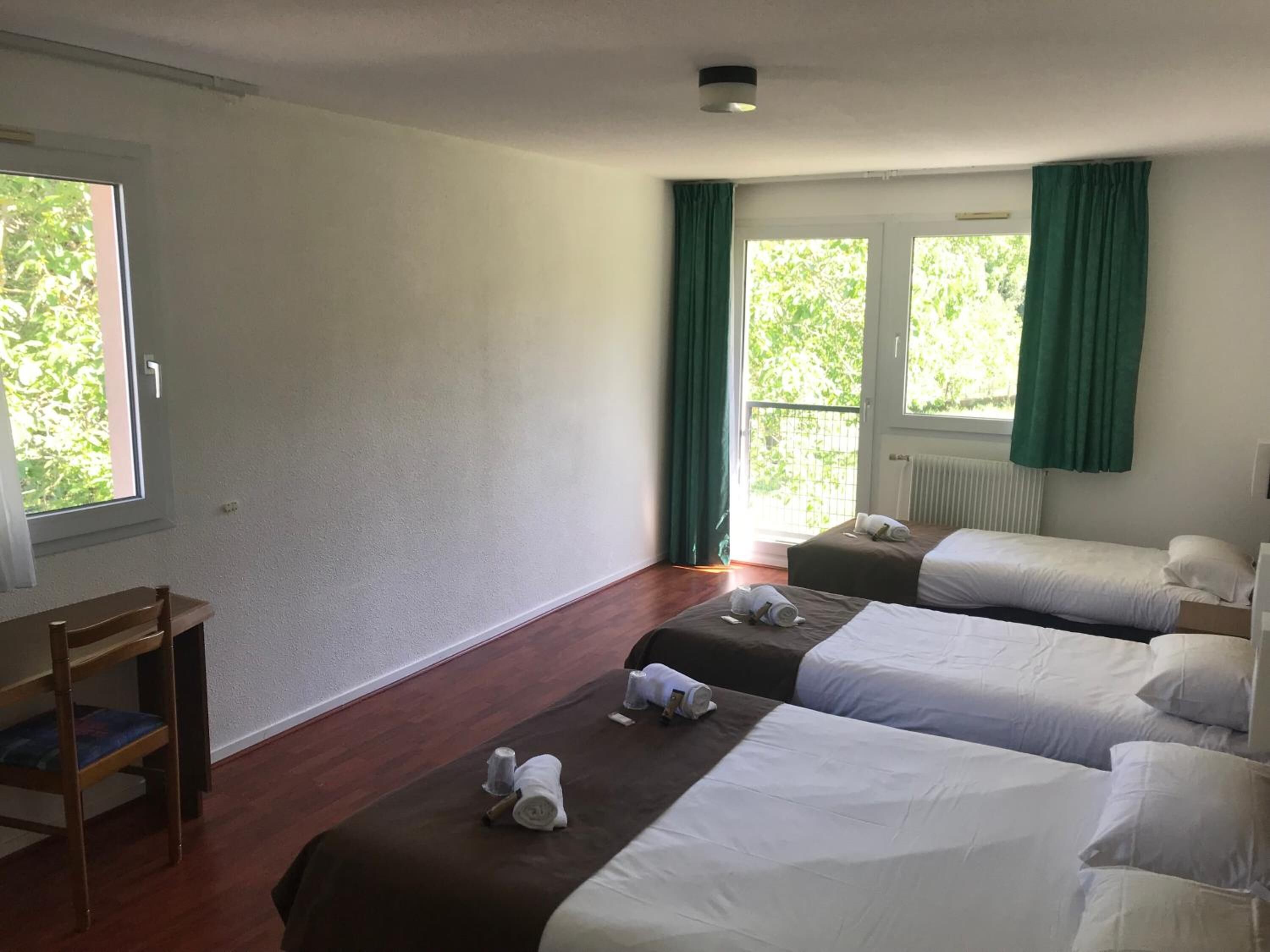 A hotel room with two beds, a wooden chair, and a window with curtains.