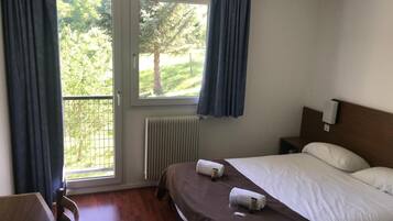 Habitación de hotel con cama, escritorio, ventana con cortinas y vista a áreas verdes.