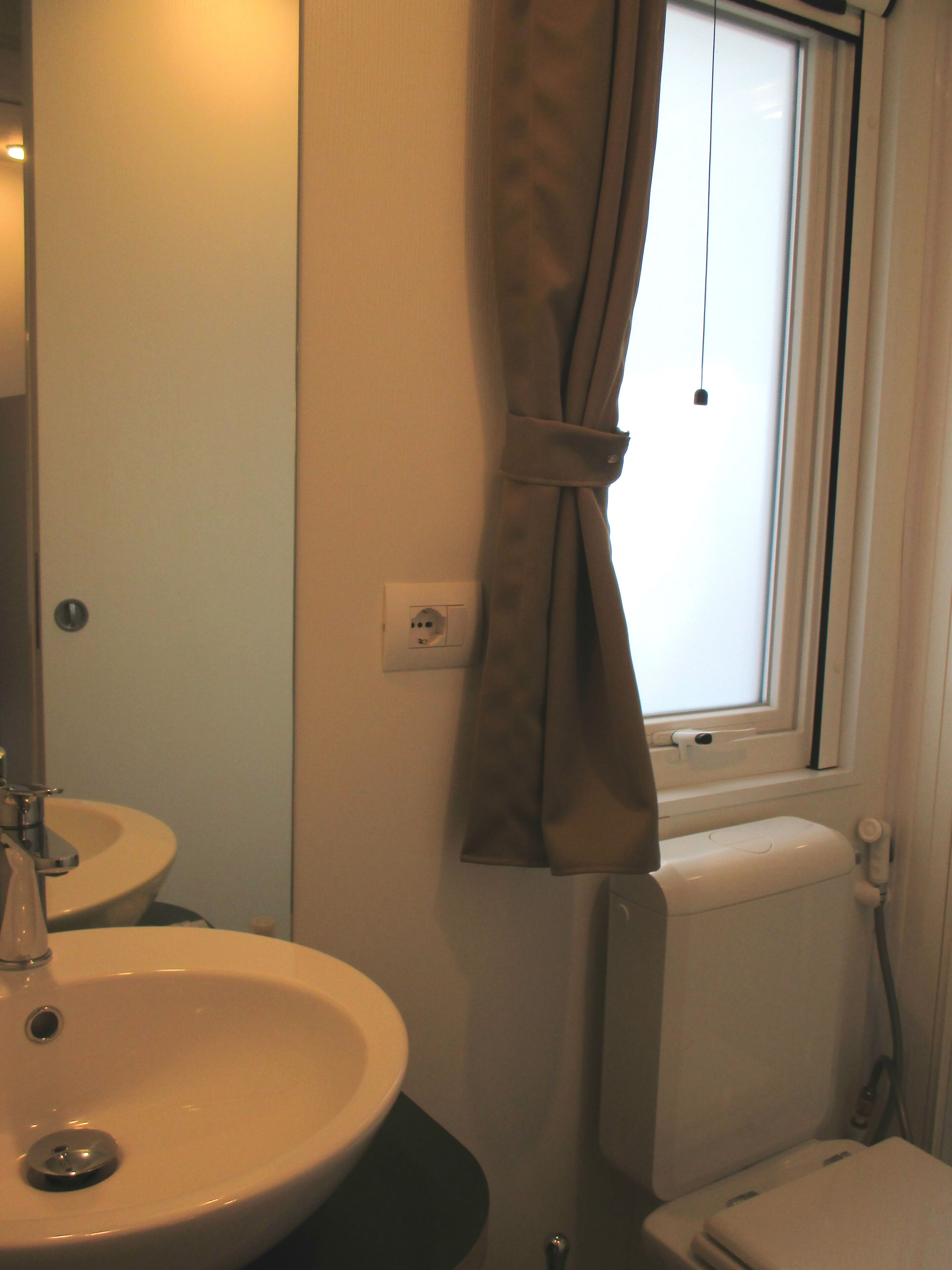 A bathroom with a sink, toilet, and window with curtains.